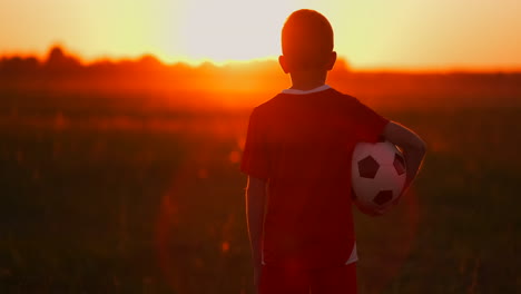 boy-with-a-ball-in-a-field-at-sunset-boy-dreams-of-becoming-a-soccer-player-boy-goes-to-the-field-with-the-ball-at-sunset.